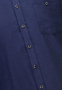 Camicia blu navy con finitura testurizzata, caratterizzata da bottoni neri, una tasca sul petto e un colletto strutturato.