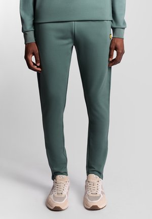 Grønne sportsjoggers lavet af glat stof, med sidesømmer, en tætsiddende form og et lille logo-patch nær hoften.
