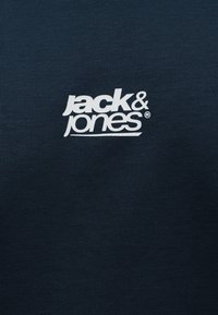 Λευκό λογότυπο "jack & jones" τυπωμένο σε σκούρο ναυτικό μπλε ύφασμα.