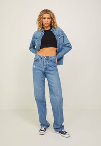 Jeans in denim blu chiaro con taglio dritto e dettagli strappati. Abbinati a una maglietta nera corta e a una camicia in denim blu chiaro.