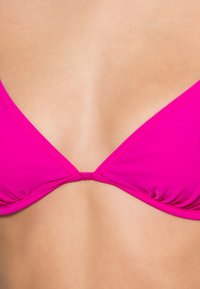 Rosa Bikini-Oberteil mit klassischem Dreiecksdesign, glatter Textur, dünnen Trägern und einer Knotenmitte.