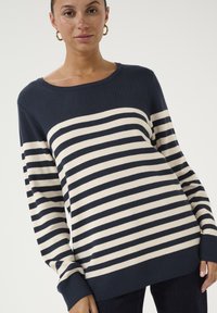 Jūras spēku un krēmkrāsas svītrains adīts džemperis ar garām piedurknēm un platajām kakla izgriezumiem, piedāvājot brīvu piegriezumu un ribota mala detaļas.