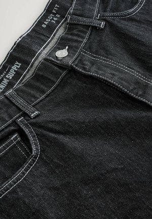 Jeans baggy noirs en denim, dotés de coutures blanches contrastantes, d'une fermeture à bouton en métal et d'une étiquette cousue sur la ceinture.