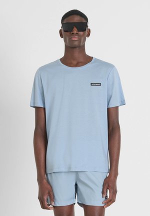 T-shirt azzurro chiaro a maniche corte con scollo rotondo e un piccolo etichetta nera sul lato sinistro del petto. Abbinato a pantaloni corti azzurro chiaro coordinati.