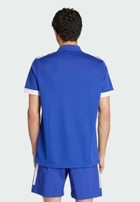 Niebieska sportowa koszulka polo z białym kołnierzem i akcentami na rękawach, wykonana z gładkiego materiału, o luźnym kroju i krótkich rękawach.