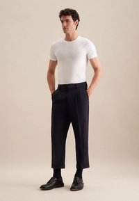 Biała dopasowana koszulka z okrągłym dekoltem, ciemnogranatowe plisowane spodnie i czarne eleganckie buty. Spodnie mają ściągany dół oraz boczne kieszenie.