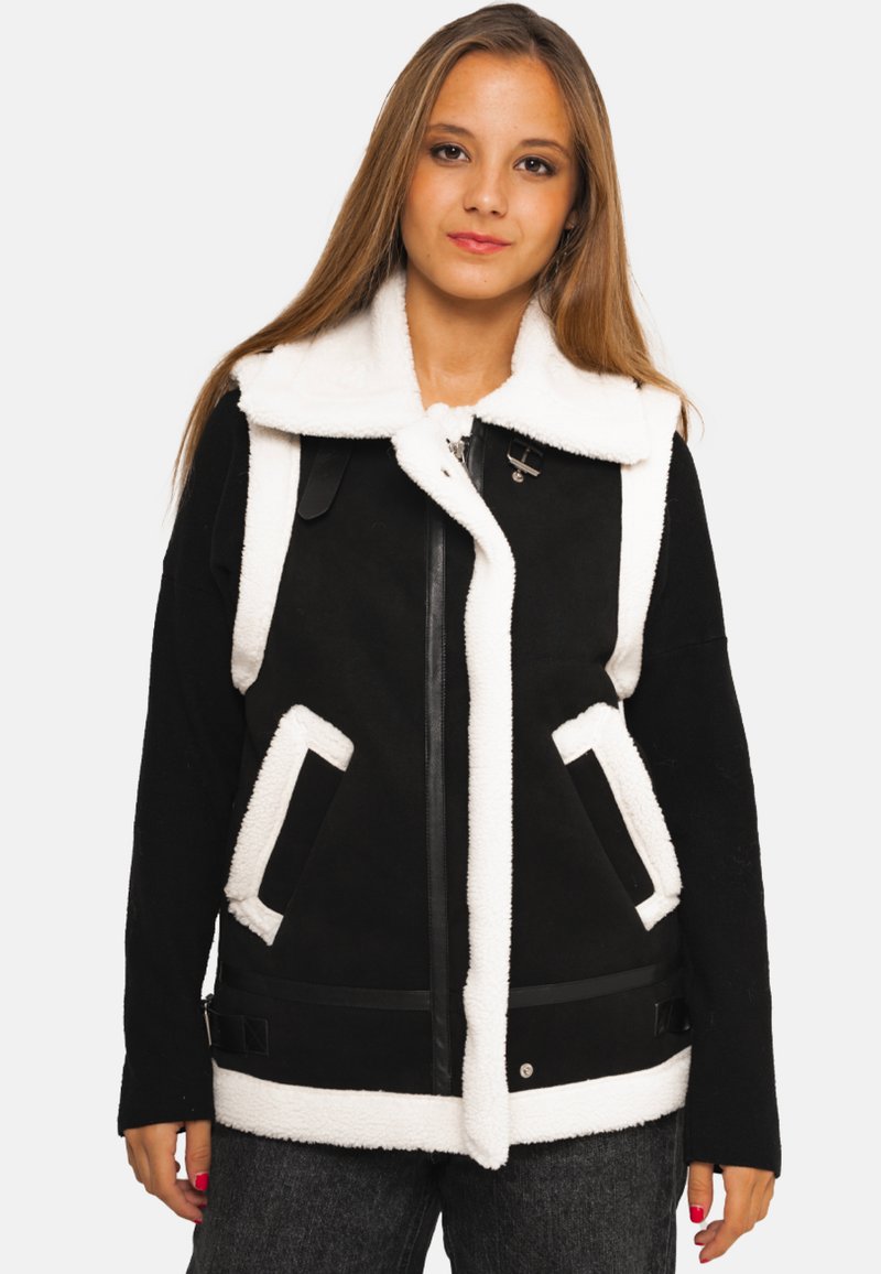 Veste sans manches isolante en noir et blanc avec un col en peau lainée, fermeture éclair, poches surdimensionnées et accents noirs élégants le long de l'ourlet et des poches.