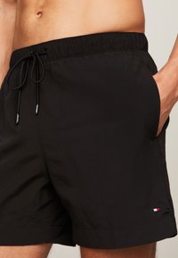 Svart badebukser laget av lett stoff. Har elastisk midjebånd med snøring, sidelommer og en liten logo. 