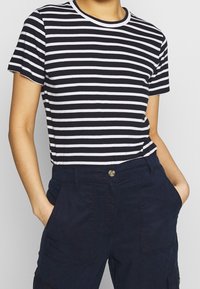 T-shirt a righe blu scuro e bianche con collo rotondo e maniche corte, abbinata a pantaloni blu scuro con tasche laterali.