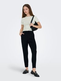 Light green short-sleeve t-shirt with embroidered details, paired with black tapered pants and black slip-on loafers, carrying a small black bag.