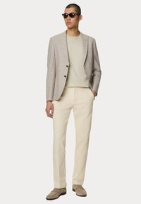 Lys beige linned blazer med to knapper, parret med en cremefarvet T-shirt og bukser i lys sandfarve. Tilbehør inkluderer mørke solbriller.