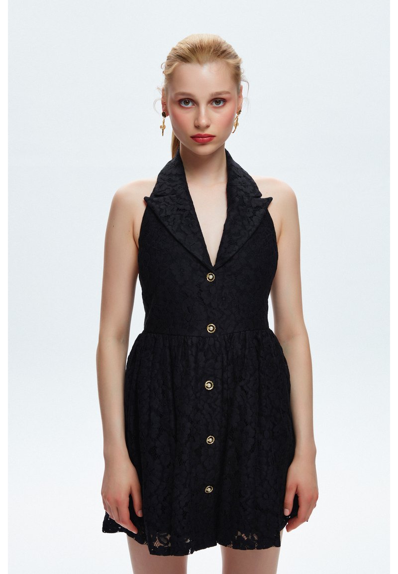 Abito in pizzo nero con scollatura a halter, colletto e bottoni dorati. Presenta un corpetto aderente e una gonna svasata. È decorato con un delicato motivo floreale.