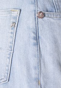 Jasnoniebieskie ogrodniczki z denimu z przednią kieszenią, wyposażone w srebrne elementy metalowe, kontrastowe przeszycia i ozdobny guzik przy kieszeni.