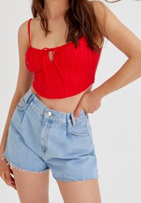 Red cropped top with a tie detail and ribbed texture, paired with light blue denim shorts featuring frayed hems and front pockets.