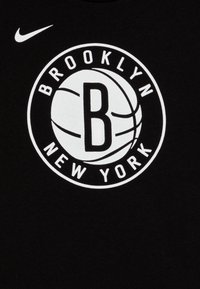 Tricou negru din bumbac, cu un grafic circular alb ce conține textul „BROOKLYN” și „NEW YORK” în jurul unei mingi de baschet și a literei „B” în centru.
