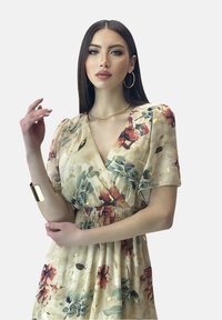 Vestido envolvente floral en color crema con flores rosas y verdes, mangas cortas abullonadas, cintura fruncida y acentos dorados. Tela suave y ligera.