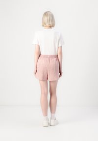 Shorts en tissu léger avec des rayures verticales rouges et blanches, dotés d'une taille élastique. Portés avec un t-shirt blanc uni et des baskets.