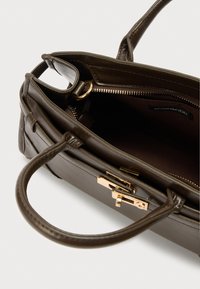 Καφέ δερμάτινη τσάντα χειρός με χρυσά μεταλλικά στοιχεία, δομημένο σχέδιο, διπλές λαβές και εσωτερική τσέπη με φερμουάρ για οργάνωση.