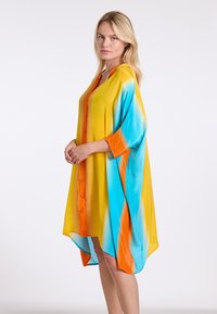 Kleurrijke, oversized jurk met gele, blauwe en oranje tinten. Soepele stof, knoopsluiting aan de voorkant, driekwartmouwen en een vloeiende zoom.