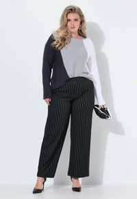 Färgblockerad tröja i marinblått, grått och vitt, parat med svarta randiga vida byxor. Modellen håller en skimrande svart clutch.