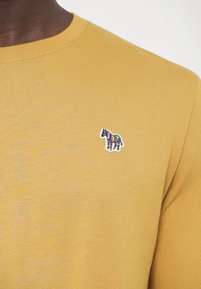 Cămașă galbenă cu mâneci lungi, textură tip plasă și un mic design brodat cu zebra pe pieptul stâng. Gât rotund.