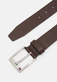 Ceinture en cuir marron avec une boucle rectangulaire en argent. Présente des accents cousus et plusieurs trous pour un ajustement. Détail du logo sur la boucle.