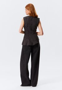 Ärmelloses schwarzes Denim-Oberteil mit tailliertem Oberteil und Peplum-Saum, kombiniert mit lockeren schwarzen Hosen, die die Steppdetails und das Rückendesign betonen.