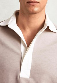 Polo shirt color marrone chiaro con colletto bianco e pattina dei bottoni. Realizzato in tessuto morbido, presenta una texture liscia e un design classico.