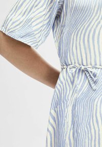 Světle modré a bílé šaty s vzorem a krátkými rukávy, které mají vázání v pase a jemnou, texturovanou tkaninu ve vlnovém designu.