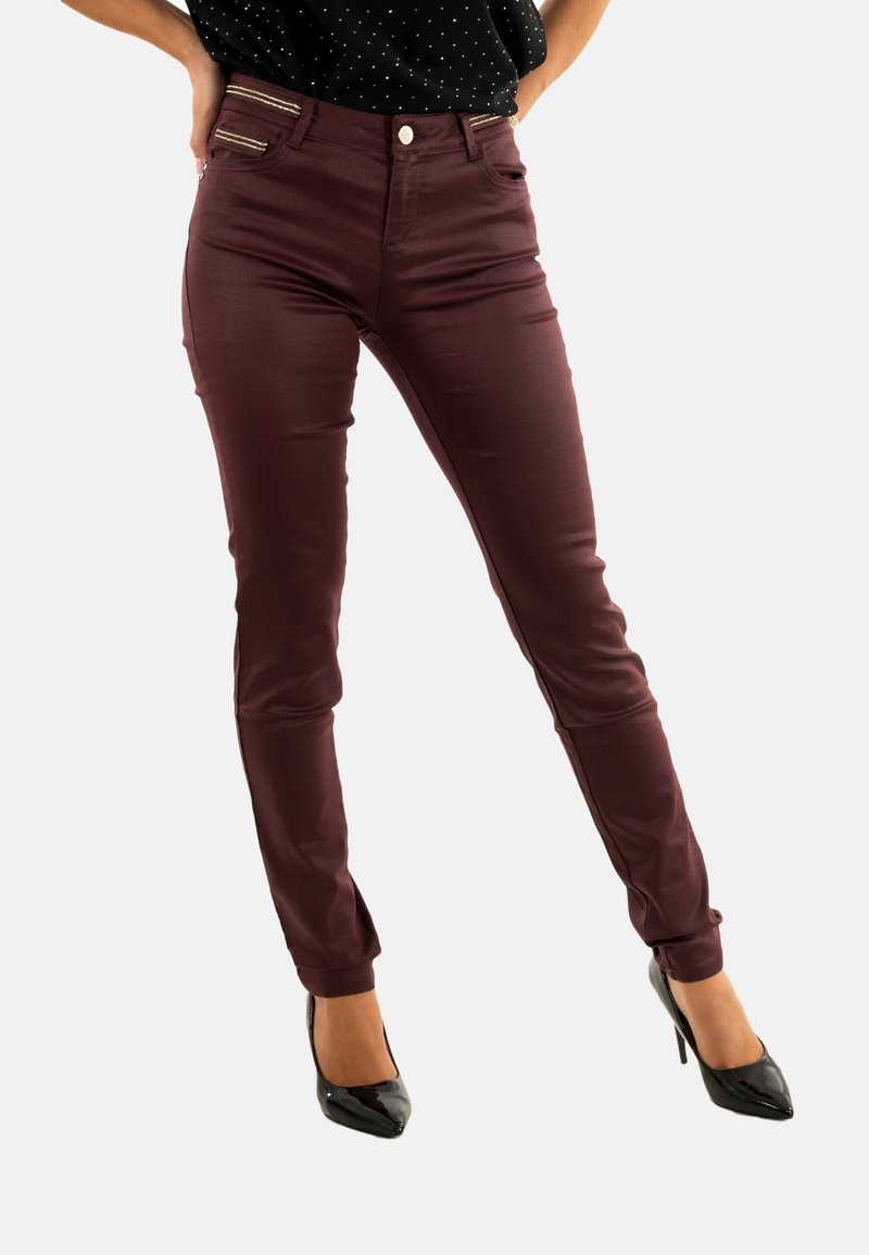 Vaqueros ajustados burdeos con una textura suave, que cuentan con dos bolsillos delanteros y detalles dorados, combinados con tacones altos negros de charol.