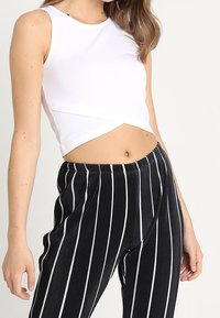 Top corto bianco senza maniche con scollo rotondo abbinato a pantaloni larghi a righe verticali bianche e nere.