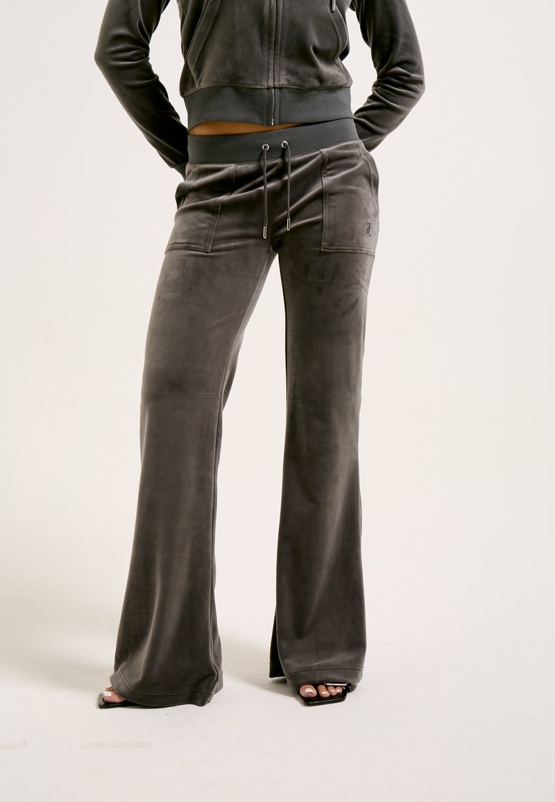 Donkergrijze, zachte stof trainingspak met uitlopende broeken. Voorzien van een hoge tailleband, een trekkoord en zijzakken voor extra functionaliteit.