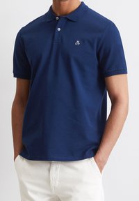 Tmavě modrá polokošile z bavlněné látky, krátké rukávy, s límečkem a třícípým zapínáním na knoflíky; na hrudi je malé vyšívané logo.