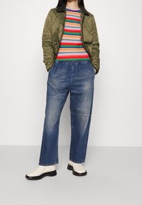 Ocieplana oliwkowa kurtka, wielokolorowy sweter w paski, luźne jasnoniebieskie dżinsy oraz białe botki za kostkę z czarną podeszwą.