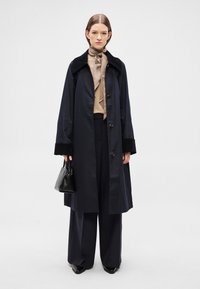 Ναυτικό μακρύ παλτό με μαύρο βελούδινο γιακά, κούμπωμα με κουμπιά και πλαϊνές τσέπες. Συνδυασμένο με μπεζ μπλούζα, φαρδιά σκούρα παντελόνια και μαύρη τσάντα.