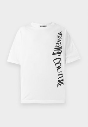 Valge ülepaisutatud t-särk, mis on valmistatud puuvillast, mustade vertikaalsete tähtedega, mis ütlevad "VERSACE JEANS COUTURE", vasakul küljel. Ümmargune kaelus.