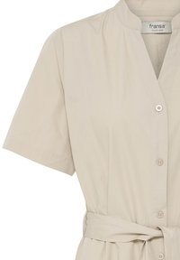 Robe beige à manches courtes avec boutons, col en V et ceinture en tissu nouée à la taille.