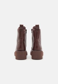 Hnědé kožené kotníkové boty se čtveratou špičkou, masivní platformou, bočními zipy a smyčkami na patě. Hladký povrch.