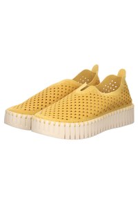 Scarpe gialle senza stringhe con design perforato, soprabotta testurizzato e suola bianca spessa caratterizzata da scanalature verticali. Nessun lacci o cinture visibili.