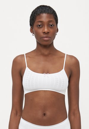 Bralette bianco con spalline sottili, caratterizzato da un motivo a maglia testurizzata e un piccolo fiocchetto rosa al centro. Tessuto liscio e design senza cuciture.