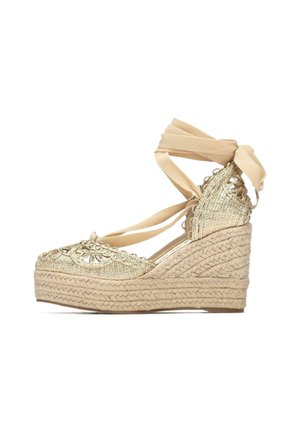 Zeppa in espadrillas intrecciate dorate con nastri beige da annodare, tomaia strutturata e tacco avvolto in juta. Dettaglio ricamato decorativo sulla punta.