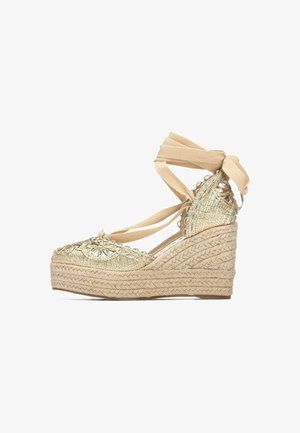 Zeppa in espadrillas intrecciate dorate con nastri beige da annodare, tomaia strutturata e tacco avvolto in juta. Dettaglio ricamato decorativo sulla punta.