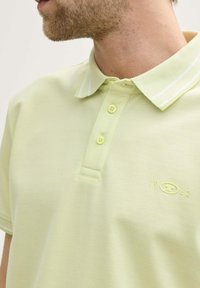 Ljust grön polo tröja i strukturerad tyg, med klassisk krage, två knappar och vita randiga detaljer på kragen. Broderad logotyp.