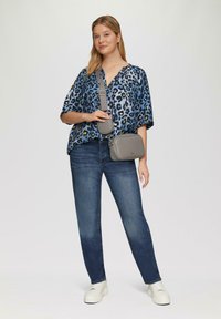 Leopardprint blauwe shirt, relaxte pasvorm; donkerblauwe spijkerbroek; grijze schoudertas; witte platform sneakers. Soepele stoftexturen en gebogen vormen.