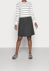 Camicia bianca a maniche lunghe con strisce nere, abbinata a una gonna grigia scura fino al ginocchio e sandali grigi chiari con doppie cinghie e fibbie.