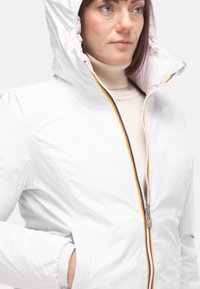 Giacca bianca isolata con cappuccio, con fodera rosa a contrasto, chiusura con zip con dettagli colorati e polsini elasticizzati.