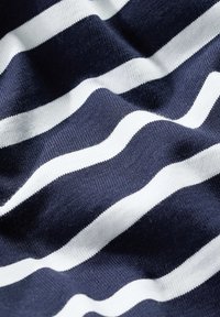 Navynsininen kangas, jossa on valkoisia raitoja, ja pehmeä, tekstuuri pinta. Raidat ovat aaltoilevia ja vaihtelevat leveyksiltään, luoden dynaamisen kuvion.