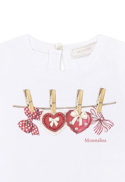 Maglietta bianca con una grafica di cuori e fiocchi appesa a mollette di legno. Dettagli notevoli includono pois, perle e decorazioni in nastro.