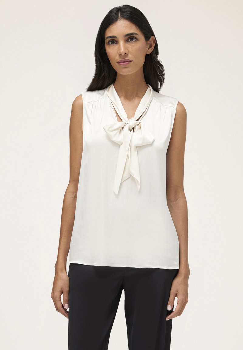 Top bianco senza maniche con un fiocco al collo, realizzato in tessuto liscio, con dettagli arricciati sulle spalle.