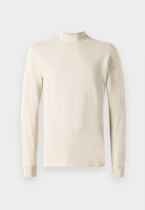 Långärmad krämfärgad polotröja gjord av mjukt bomullstyg, med en figurnära design och ribbad halsringning samt rak fåll.